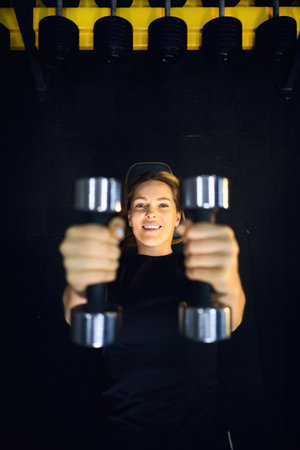 Top view portrait of A beautiful athletic middle-aged blond woman in sportswear in the fitness room raises dumbbells lying downの写真素材