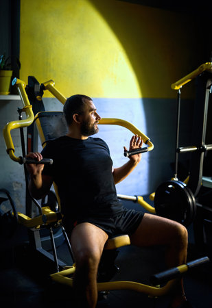 Motivated middle aged man having workout on chest press machine in gym, pushing weight while sitting...