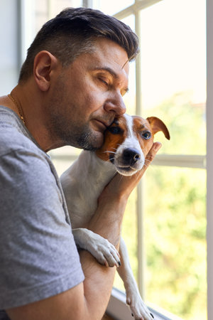 Adorable man and lovable, pretty puppy Jack Russel terrier near the window. Close-up, indoor. Day light. Concept of care, education, obedience training and raising petsの写真素材