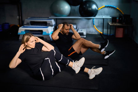 Two middle-aged athletes exercising together in fitness. Attractive handsome sportsman and sportswomen doing sit-up cardio workout to maintain strong muscle for health care in gym club.の写真素材