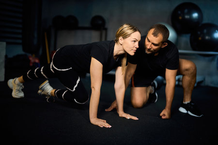 Young sportswoman doing push-ups during exercise class with a coach in health club.の写真素材