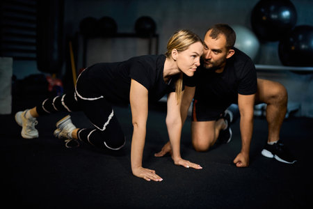 Young sportswoman doing push-ups during exercise class with a coach in health club.の写真素材