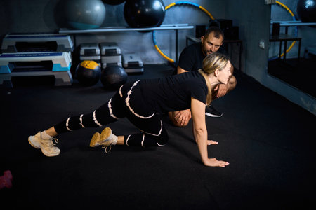Young sportswoman doing push-ups during exercise class with a coach in health club.の写真素材