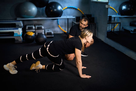 Young sportswoman doing push-ups during exercise class with a coach in health club.の写真素材