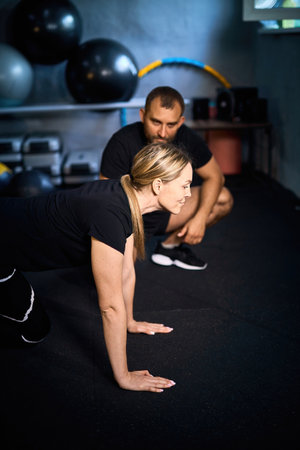 Young sportswoman doing push-ups during exercise class with a coach in health club.の写真素材