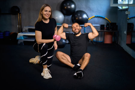 Happy athletic couple flexing their muscles after hard working out in a gym and looking at camera, smiling.の写真素材