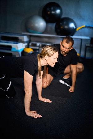 Young sportswoman doing push-ups during exercise class with a coach in health club.の写真素材