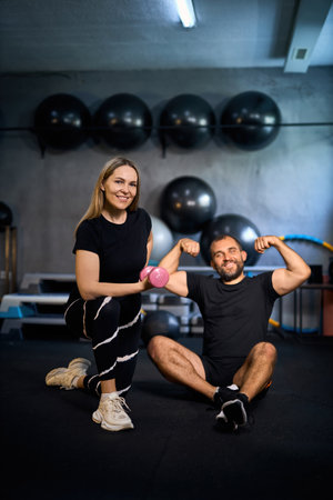 Happy athletic couple flexing their muscles after hard working out in a gym and looking at camera, smiling.の写真素材