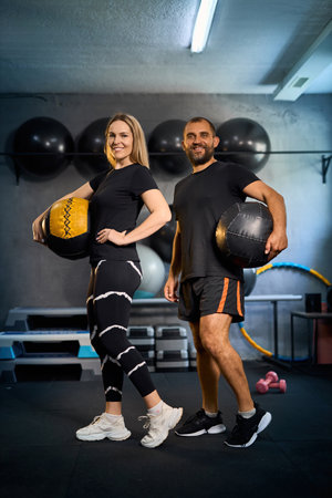 Sporty couple exercising together in gym. Handsome man assisting beautiful girl while doing exercises with medicine ball in GYM.の写真素材