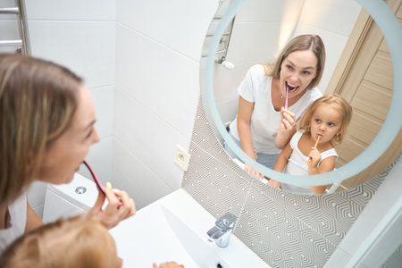Woman and child brushing each other's teeth with a toothbrush in a bathroom. The child is potentially learning how to brush her own teeth. Happy family. Dental careの写真素材
