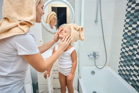 Happy mom puts a towel on girl kid head. Young mother with cute little daughter in the bathroom. Healthcare and family concept. Cheerful beauty day at home.の写真素材