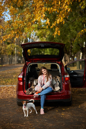 A teenage girl and a Jack Russel terrier dog are sitting in the trunk of a car. Autumn travel by car with a pet.の写真素材