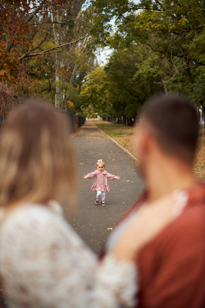 Parents, Funny daughter running to mom and dad. Active family playing in park with their daughters. Happy family, warm autumn day in park. Family, natureの写真素材