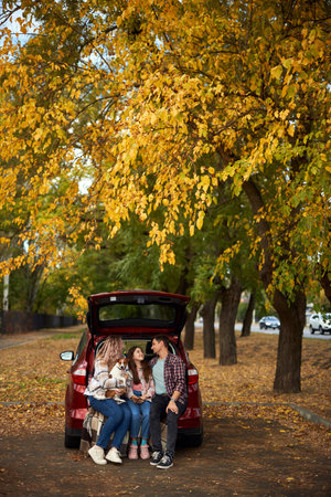 Happy parents with daughter and cute dog Jack Russel terrier sitting in car trunk on autumn day. Long auto journey break.の写真素材