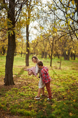 Beautiful happy mother playing with her kids in sunny autumn parkの写真素材