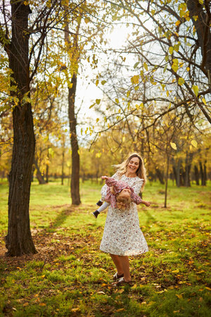 Beautiful happy mother playing with her child in sunny autumn parkの写真素材