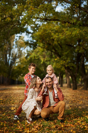 Happy family walking on green grass strewn with fallen leaves in Park in autumn. Parents, two children are walking in park hug and laugh. Family, child, walk through Autumn Park.の写真素材