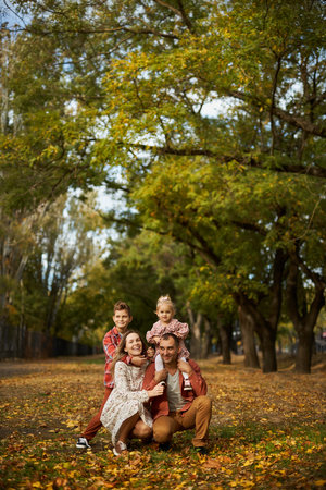 Happy family walking on green grass strewn with fallen leaves in Park in autumn. Parents, two children are walking in park hug and laugh. Family, child, walk through Autumn Park.の写真素材