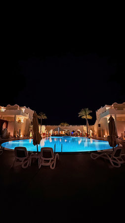 Night illumination. Beautiful empty swimming pool area, palm trees, lamps, colored lights, and hotel buildings in the background.の写真素材