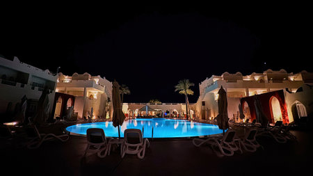 Night illumination. Beautiful empty swimming pool area, palm trees, lamps, colored lights, and hotel buildings in the background.の写真素材