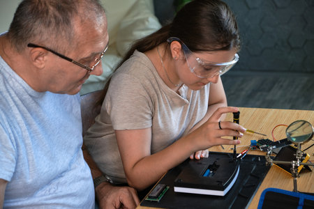 Grandfather and granddaughter work together on an electronics project at a table. Ideal for family,...