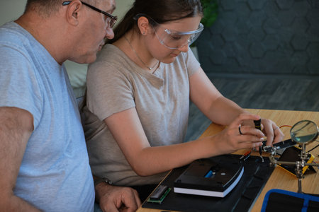 Grandfather and granddaughter work together on an electronics project at a table. Ideal for family, education, and DIY themesの写真素材