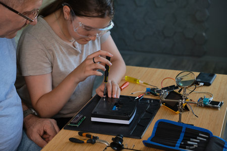 Grandfather and granddaughter work together on an electronics project at a table. Ideal for family, education, and DIY themesの写真素材