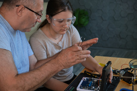 Grandfather teaches his granddaughter how to repair electronic devices at home, fostering learning and skill development. Ideal for educational, family, and DIY repair themesの写真素材