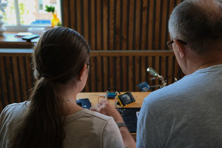 Grandfather teaches his granddaughter how to repair electronic devices at home, fostering learning and skill development. Ideal for educational, family, and DIY repair themesの写真素材