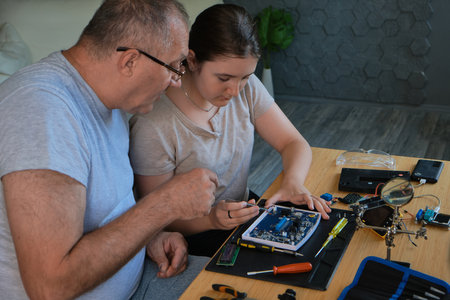 Grandfather and granddaughter work together on an electronics project at a table. Ideal for family, education, and DIY themesの写真素材