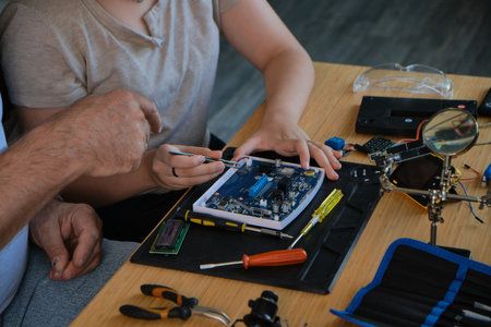 Grandfather teaches his granddaughter how to repair electronic devices at home, fostering learning and skill development. Ideal for educational, family, and DIY repair themesの写真素材