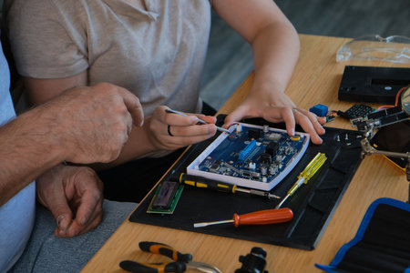 Grandfather teaches his granddaughter how to repair electronic devices at home, fostering learning and skill development. Ideal for educational, family, and DIY repair themesの写真素材