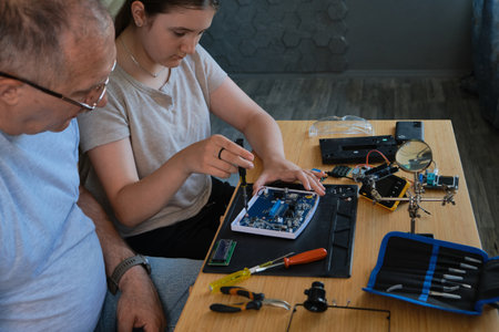 Grandfather and granddaughter work together on an electronics project at a table. Ideal for family, education, and DIY themesの写真素材