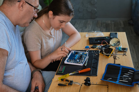 Grandfather and granddaughter work together on an electronics project at a table. Ideal for family, education, and DIY themesの写真素材