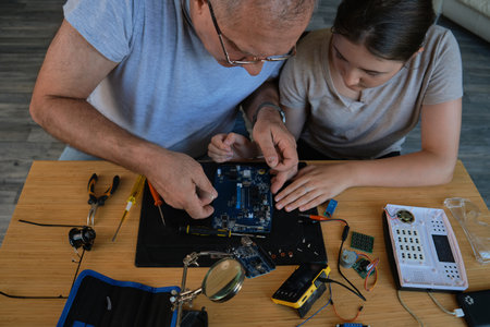 Grandfather teaches his granddaughter how to repair electronic devices at home, fostering learning and skill development. Ideal for educational, family, and DIY repair themesの写真素材