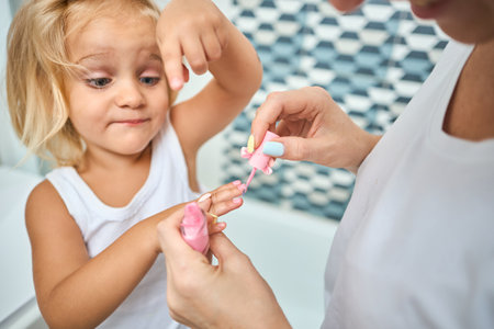 Young mother and daughter in a bathroom happy smiling make hand manicure. Skin care concept in bathroomの写真素材