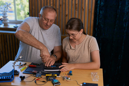 Grandfather and granddaughter work together on an electronics project at a table. Ideal for family, education, and DIY themesの写真素材
