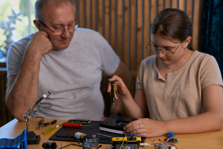 Grandfather and granddaughter work together on an electronics project at a table. Ideal for family, education, and DIY themesの写真素材