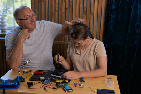 Grandfather Praises for successes his granddaughter for working together on an electronics project at a table. Ideal for family, education, and DIY themesの写真素材