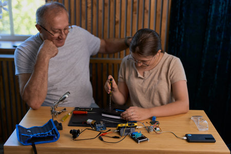 Grandfather teaches his granddaughter how to repair electronic devices at home, fostering learning and skill development. Ideal for educational, family, and DIY repair themesの写真素材