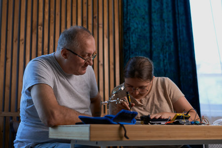 Grandfather teaches his granddaughter how to repair electronic devices at home, fostering learning and skill development. Ideal for educational, family, and DIY repair themesの写真素材