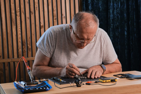 Mature Men wearing denim shirt working with electronic components at his home officeの写真素材