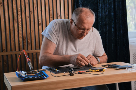 Mature Men wearing denim shirt working with electronic components at his home officeの写真素材