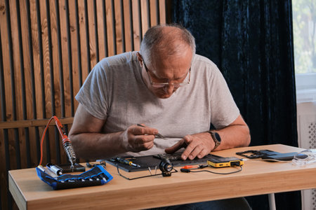 Mature Men wearing denim shirt working with electronic components at his home officeの写真素材
