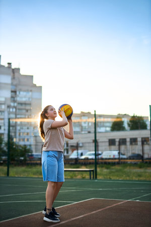 Sports and basketball. Girl throwing a basketball ball into the hoop while playing on an outdoor court In the rays of the sunset. Sports conceptの写真素材