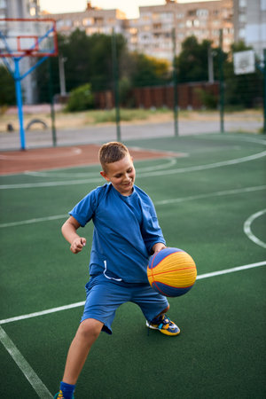 Sports and basketball. Boy in a blue tracksuit playing basketball, leading the ball. Residential urban area in the background. Copy spaceの写真素材
