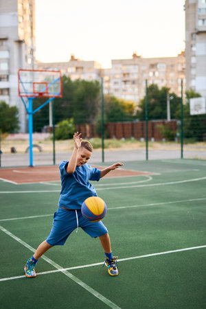 Sports and basketball. Boy in a blue tracksuit playing basketball, leading the ball. Residential urban area in the background.の写真素材