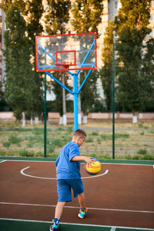 Sports and basketball. Boy in a blue tracksuit playing basketball, leading the ball. Residential urban area in the background. Copy spaceの写真素材