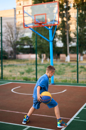 Sports and basketball. Boy in a blue tracksuit playing basketball, leading the ball. Residential urban area in the background. Copy spaceの写真素材