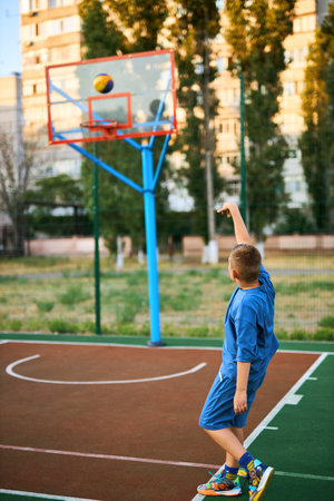 Sports and basketball. Boy in a blue tracksuit throwing a basketball ball into the hoop while playing on an outdoor court. Residential urban area in the background. Sports conceptの写真素材
